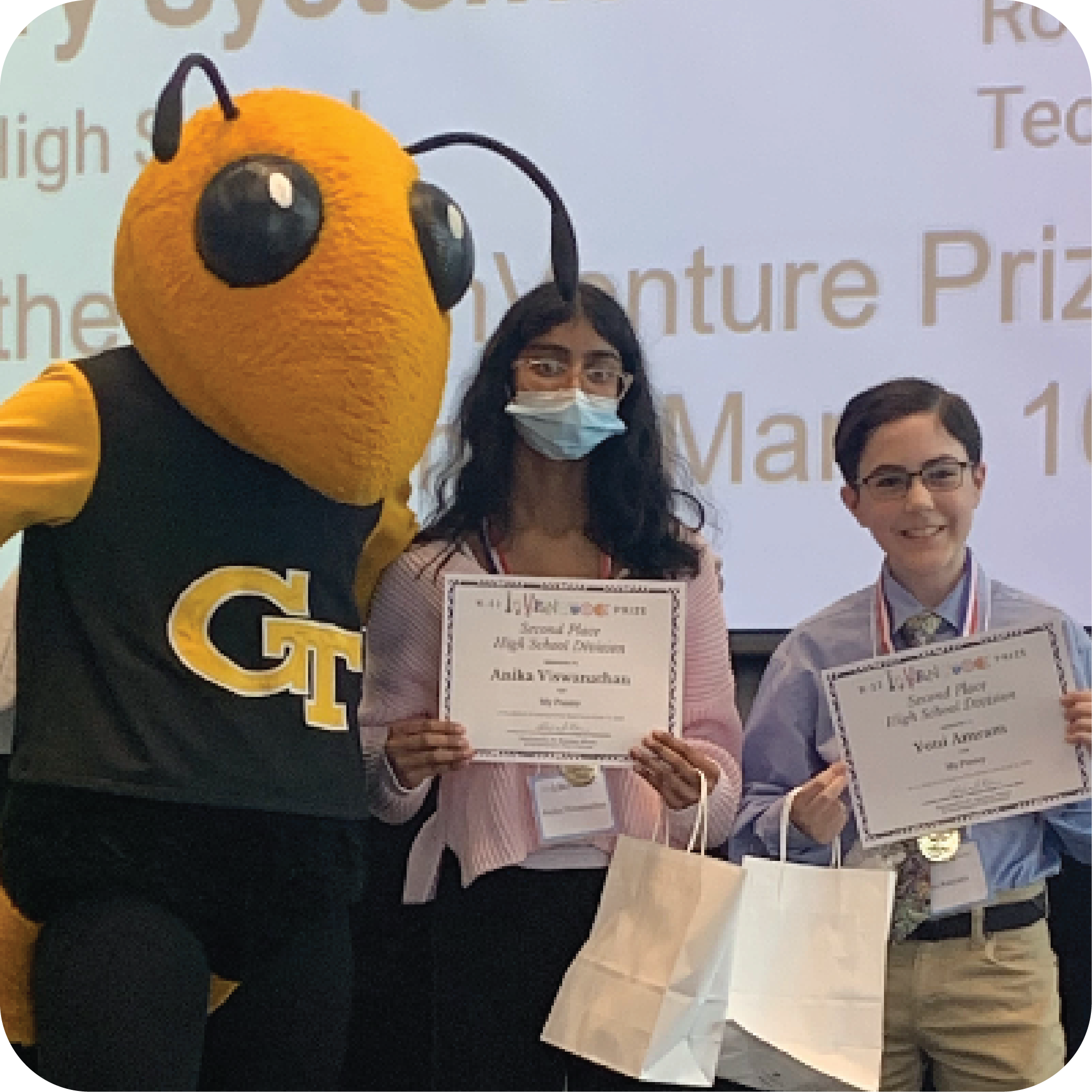 Two smiling students holding certificates and standing next to Buzz (Georgia Tech's yellowjacket mascot).